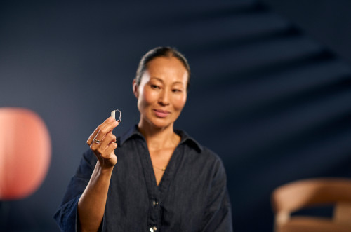 A woman smiling while holding a hearing aid