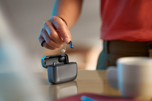 A woman picks up a hearing aid out of its charger